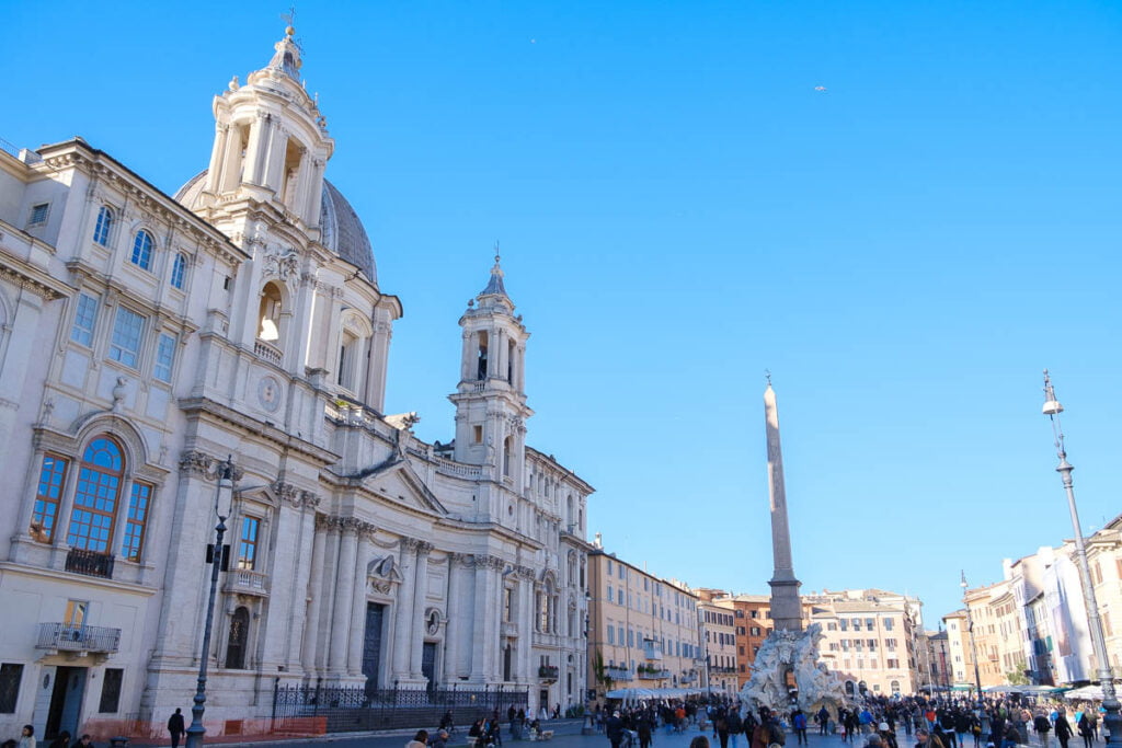 a large white building with a tower and people walking around - Leave you bags